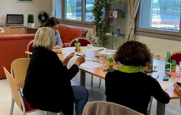 Featured Image: AliVe workshop participants are sitting around a table filling out the participant survey.